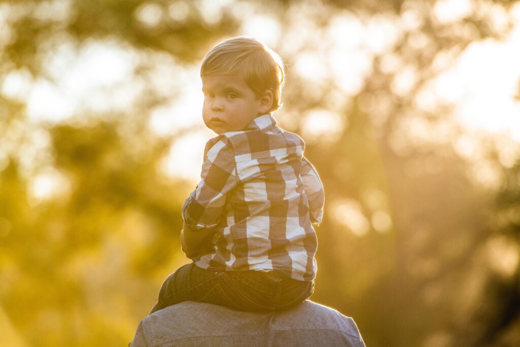 Backlit photo of a young child on his fathers shoulders San Diego Photographer