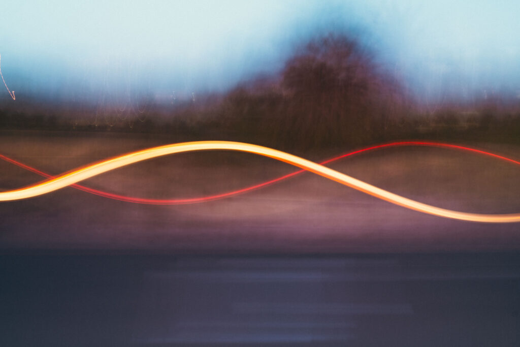 abstract photo of light passing in front of a blurry silhouette of trres and a road