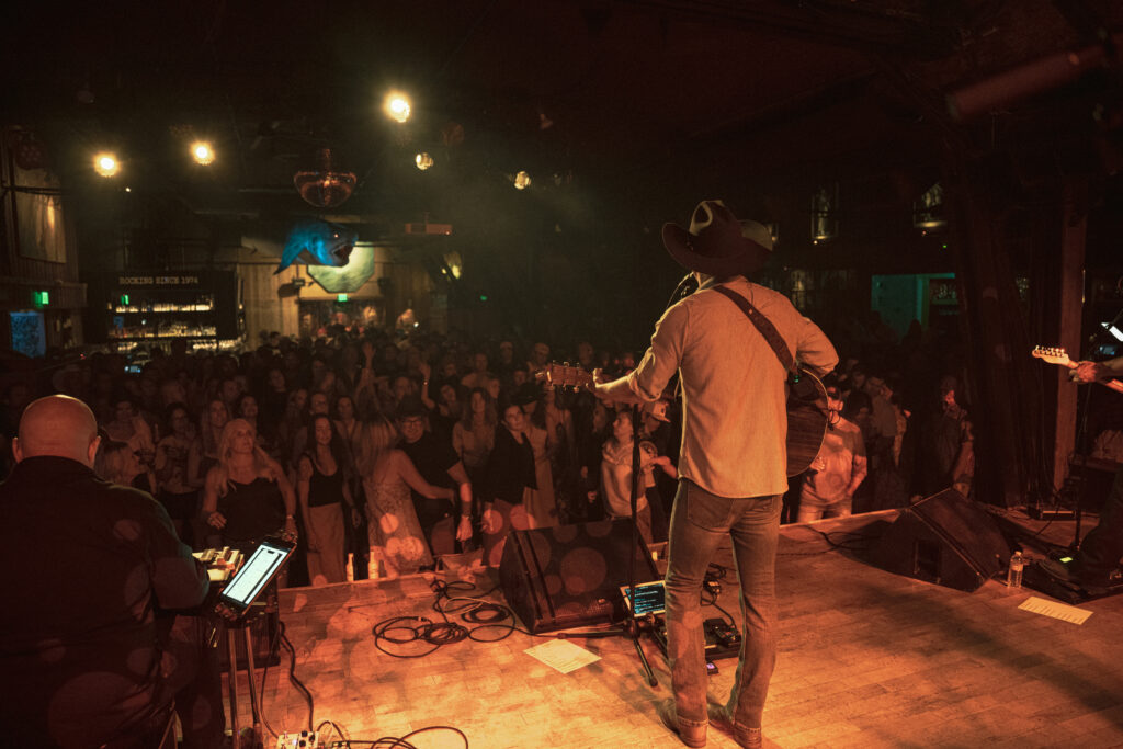 wide shot from behind a country music artist performing at the belly up showing him and the crowd 
