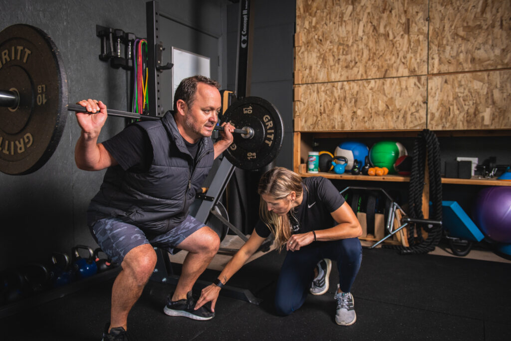 Man performing a back squat with a physical therapist making sure his form is good. Rob wessels fitness photography